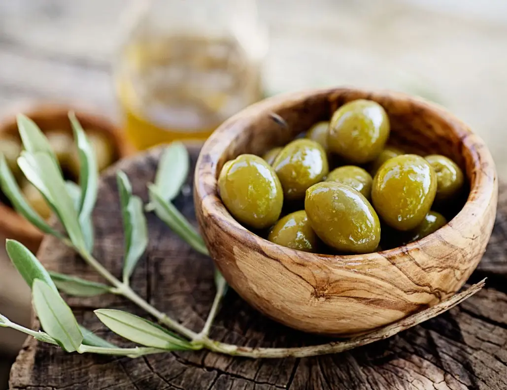 a wooden bowl full of olives and a olive leaves